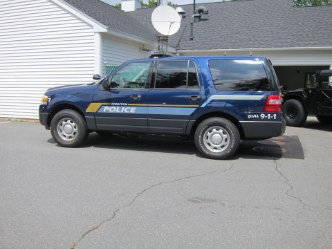2001 Ford Crown Victoria - A blue police SUV, possibly a Ford Expedition, is parked outside a building with a satellite dish mounted on its roof.