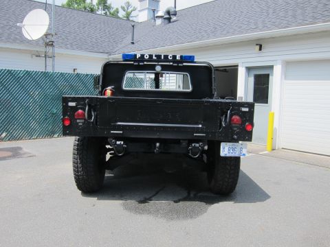 2001 Ford Crown Victoria - Rear view of a black military-style flatbed truck lettered POLICE with light bar, dual taillights and large off-road tires.