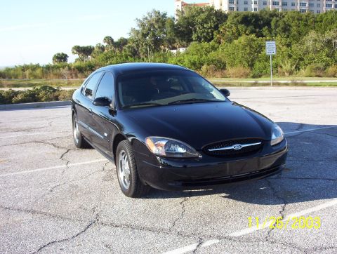 2003 Ford Taurus - A black 2003 Ford Taurus is parked in a lot with a body of water and buildings in the background.