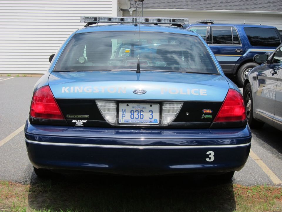 Rear of a blue 2001 Ford Crown Victoria police car with 'KINGSTON POLICE' on the trunk lid and license plate M 836 3