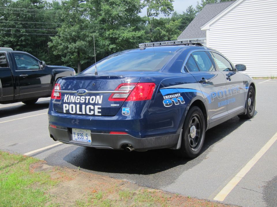 Blue Ford Police Interceptor with "KINGSTON POLICE" text, parked next to a black pickup truck