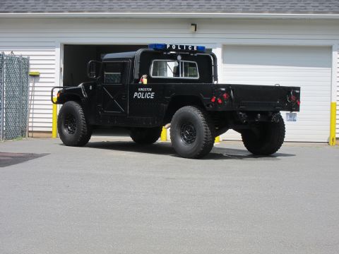 2001 Ford Crown Victoria - A black Humvee police truck is parked outside a building with its doors closed and lights on.