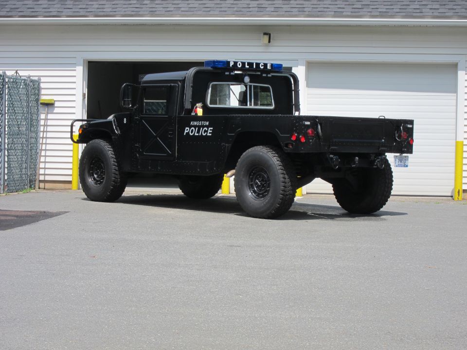 Black Humvee with POLICE markings and light bar parked in front of a garage
