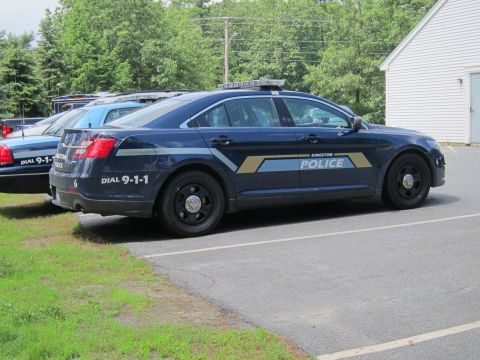 2001 Ford Crown Victoria - A Kingston Police car is parked next to another police vehicle, showing its side profile with official markings and emergency lights on the…
