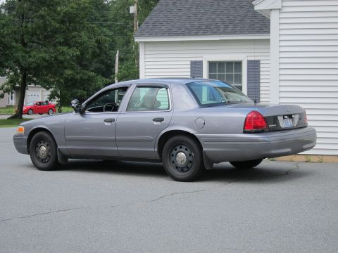 2001 Ford Crown Victoria - A gray Ford Crown Victoria police car is parked next to a white building.