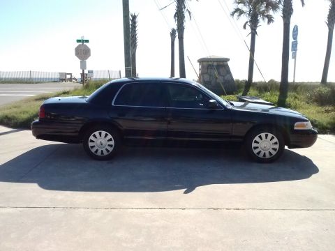 2008 Ford Crown Victoria - Side view of a black 2008 Ford Crown Victoria parked outdoors with palm trees and a stop sign visible.
