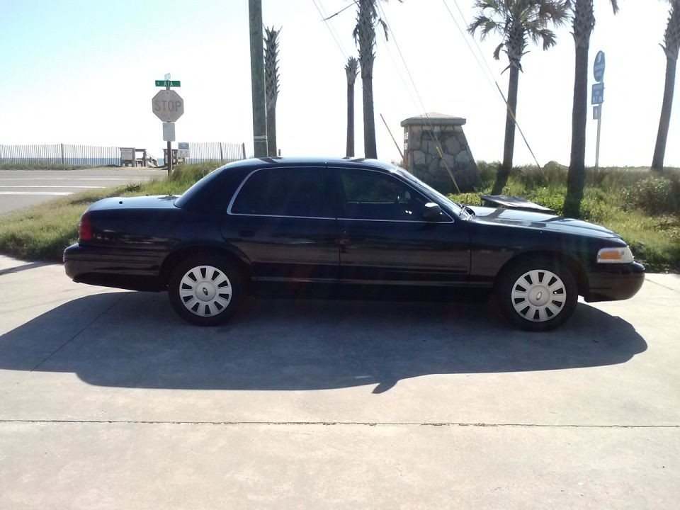 Black 2008 Ford Crown Victoria parked on a concrete surface near a beach
