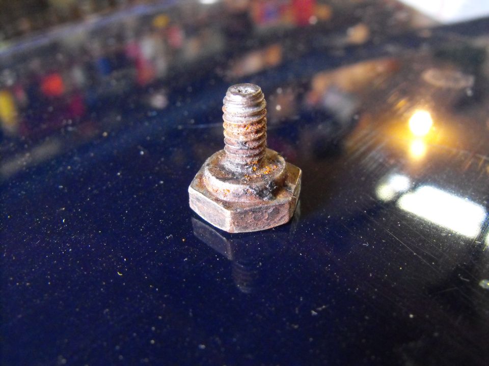 Rusty hex-head bolt standing upright on a glossy dark blue surface