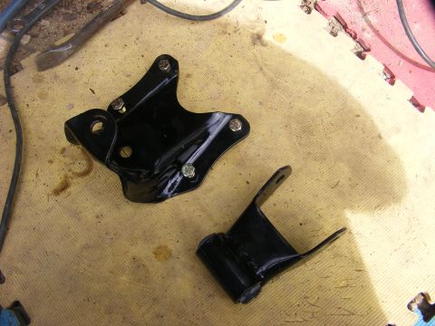 1996 Ford Bronco - Two black metal suspension components are laid out on a textured yellow surface, with tools visible in the background.