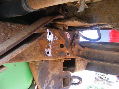 1996 Ford Bronco - Close-up view of heavily rusted frame and suspension parts, showing drilled holes and a trailer hitch receiver.