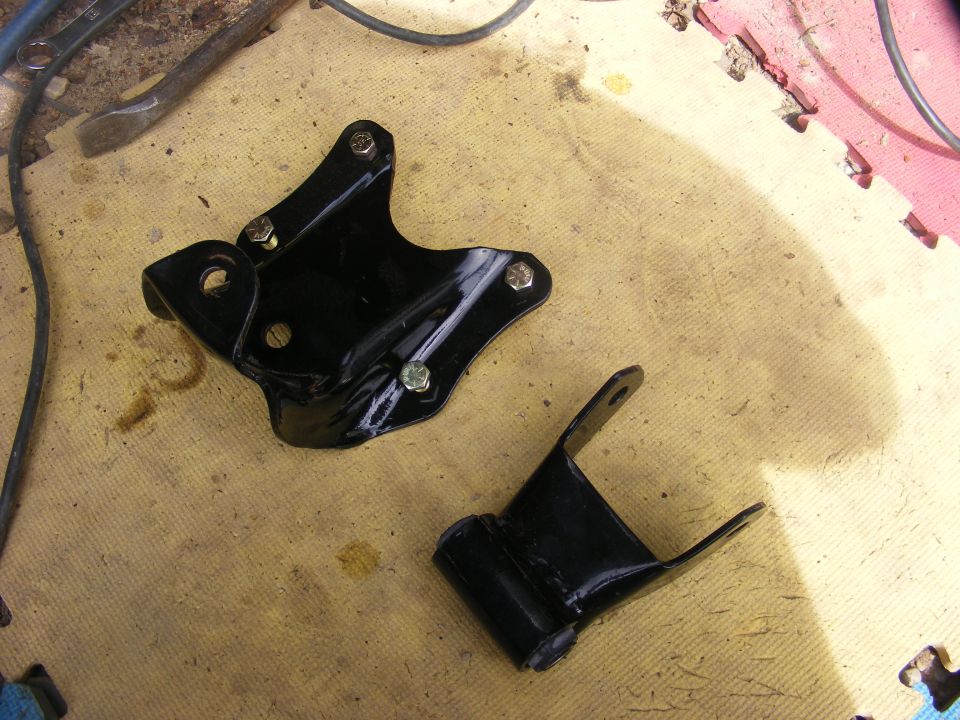Two black metal brackets with bolts on a yellow mat