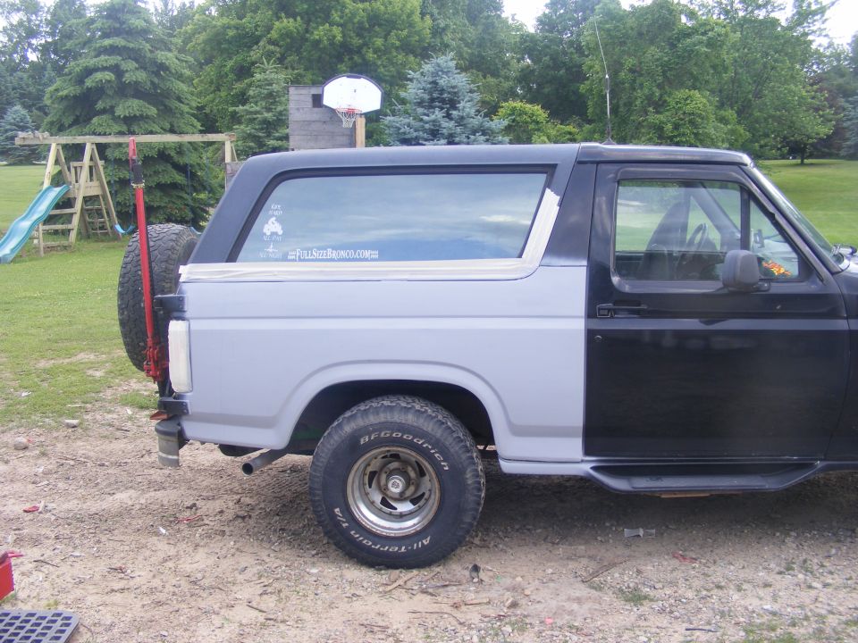 Side view of a two-tone Ford Bronco, primer gray rear, black front, with spare tire mounted externally