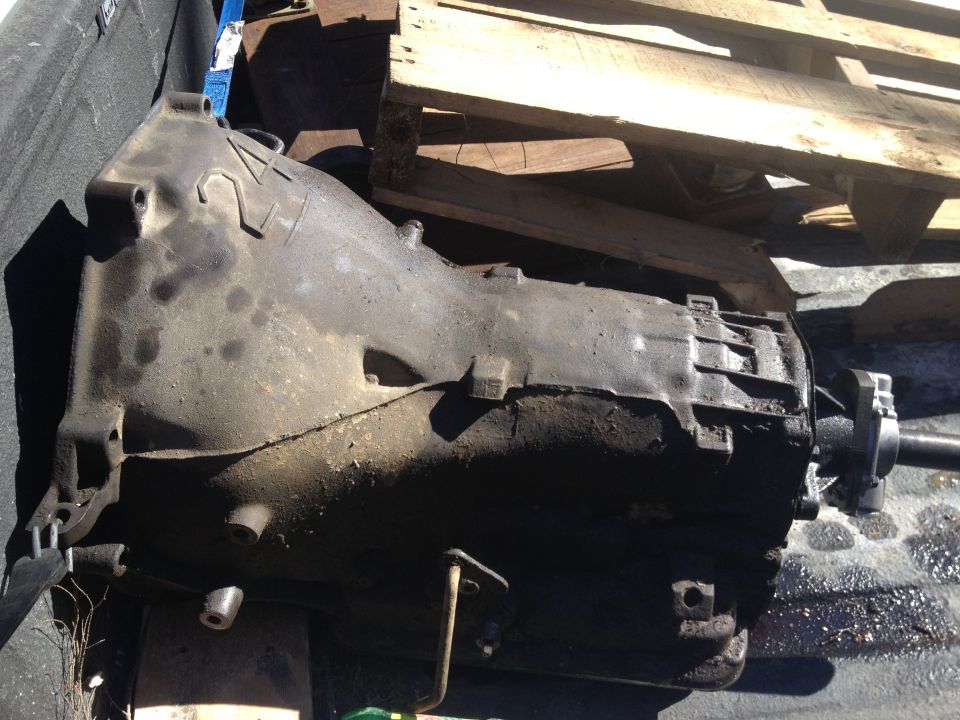 Dirty automatic transmission, possibly from a truck or SUV, resting on a pallet