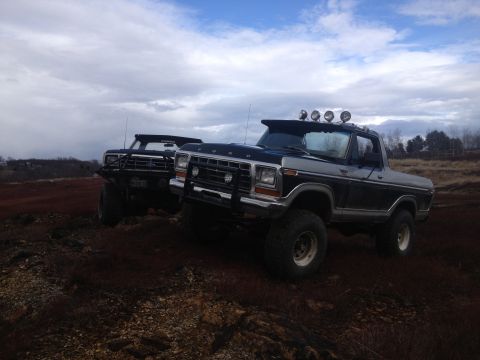 1979 Ford Bronco - Two modified 1979 Ford Broncos are seen parked on uneven terrain under a cloudy sky.