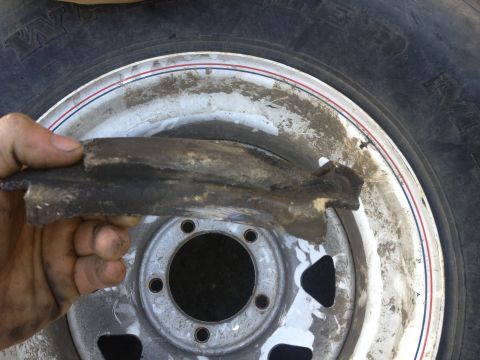 1979 Ford Bronco - A person holds a damaged part in front of a wheel rim and tire.