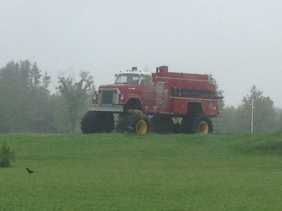 Red fire truck with oversized tires and yellow rims parked on a grassy hill