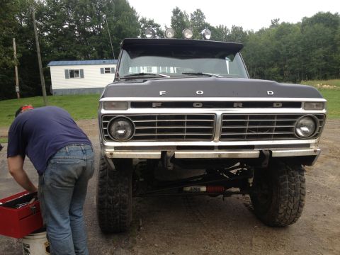 1979 Ford Bronco - A man works on a black 1979 Ford Bronco parked outdoors.
