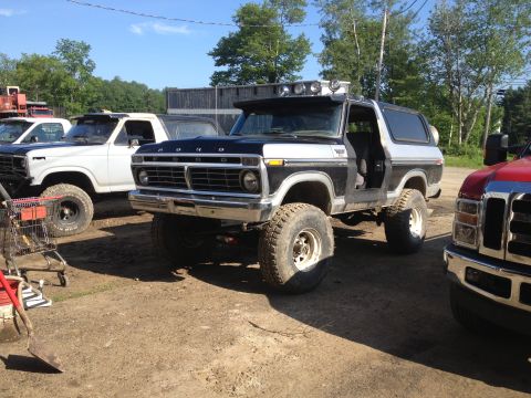 1979 Ford Bronco - This lifted Ford Bronco is parked outdoors next to other trucks on a sunny day.