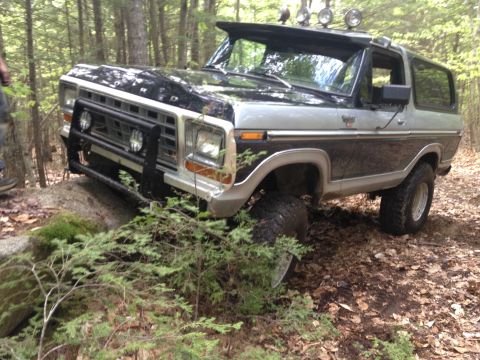1979 Ford Bronco - A two-tone black and silver Ford Bronco navigates a rocky, wooded trail.