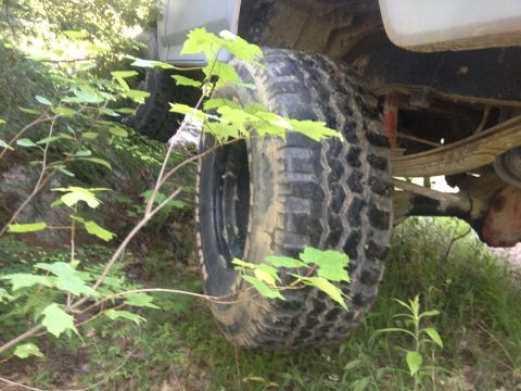 1979 Ford Bronco - A close-up view of a vehicle's off-road tire and suspension system, surrounded by greenery.