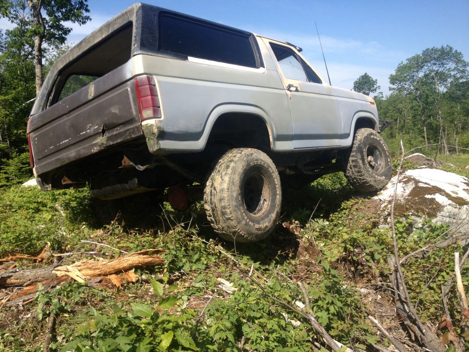 Gray 1979 Ford Bronco with off-road tires climbing over rocks