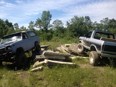 1979 Ford Bronco - Two Ford Broncos are shown off-roading over concrete debris on a sunny day.