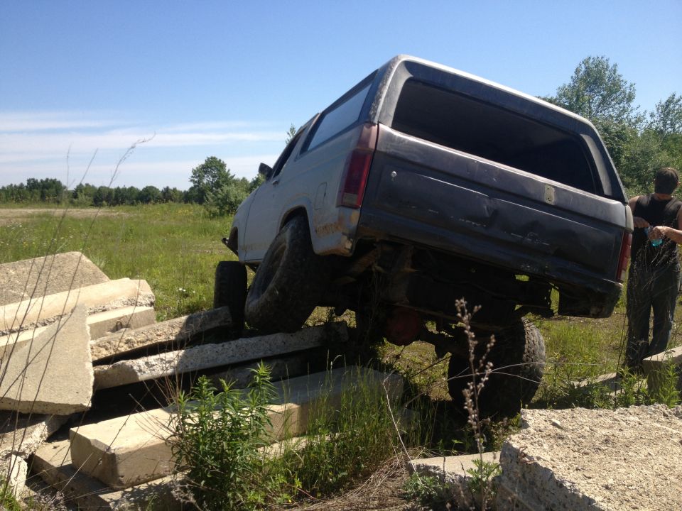 1978 Ford Bronco with lifted suspension driving over concrete blocks, person standing nearby