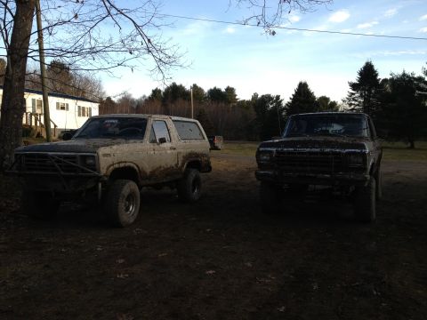 1979 Ford Bronco - Two Ford Broncos, one tan and one dark, are covered in mud in an outdoor setting.