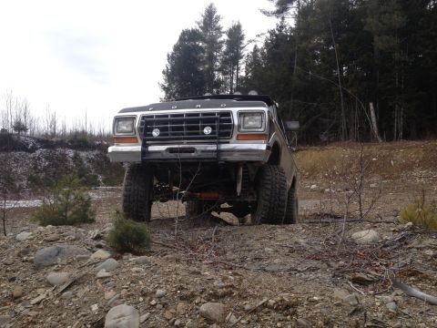 1979 Ford Bronco - This lifted Ford truck is parked on a rough, outdoor terrain with trees in the background.