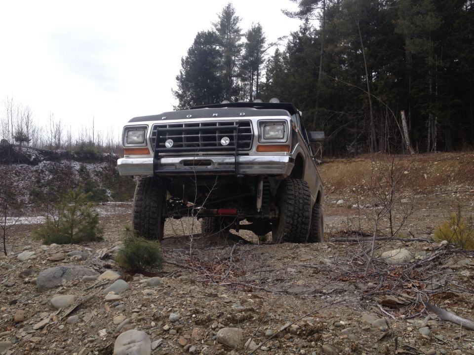 Ford truck with a brush guard and lifted suspension on a rocky, wooded trail