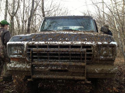 1979 Ford Bronco - Muddy 1979 Ford Bronco stuck in the woods, front grille and headlights visible.