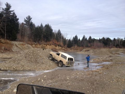 1979 Ford Bronco - A tan SUV navigates a challenging off-road terrain with a person observing the action.