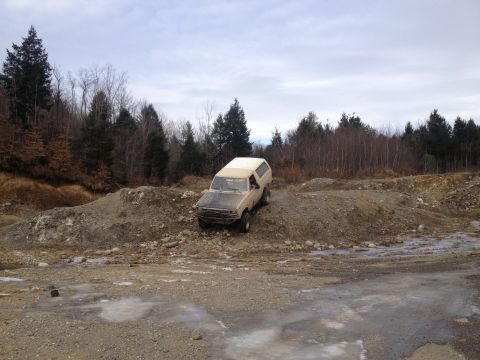 1979 Ford Bronco - A four-wheel drive vehicle navigates a rough, muddy terrain with trees in the background.
