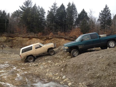 1979 Ford Bronco - Two trucks navigate a muddy, rocky incline under a cloudy sky.