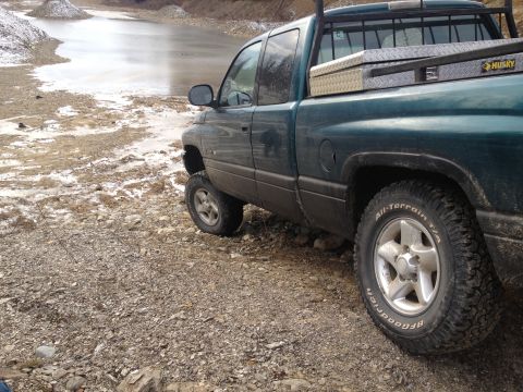 1979 Ford Bronco - A dark green pickup truck is parked on a rocky, wet surface next to a body of water with ice.
