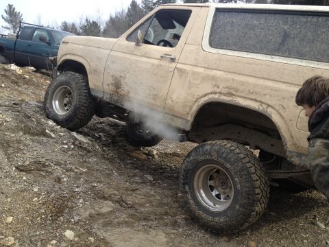 1979 Ford Bronco - A lifted SUV navigates a steep, rocky incline, kicking up dust and exhaust.