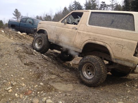 1979 Ford Bronco - A tan SUV navigates a muddy incline, with another dark-colored truck behind it.