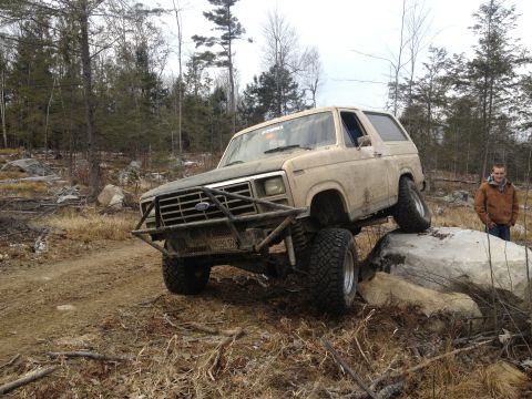 1979 Ford Bronco - A tan Ford Bronco navigates an off-road obstacle course with a man standing nearby.