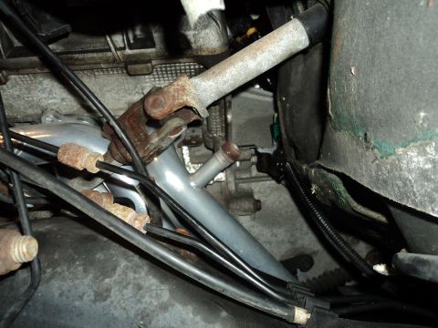 2004 Mercury Grand Marquis - Engine bay view shows a rusty steering column U-joint and associated metal pipes and wiring harnesses.