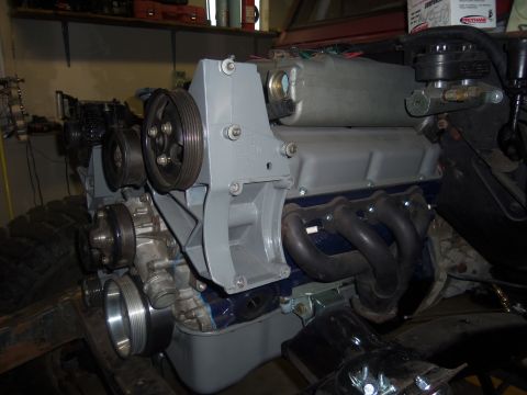 1968 Ford Bronco - Close-up view of an engine block, an exhaust manifold, pulleys, and belts, likely during a rebuild or modification.