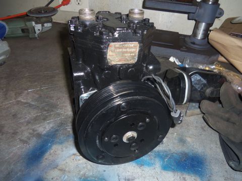 1968 Ford Bronco - A black automotive air conditioning compressor sits on a workbench with tools in the background.