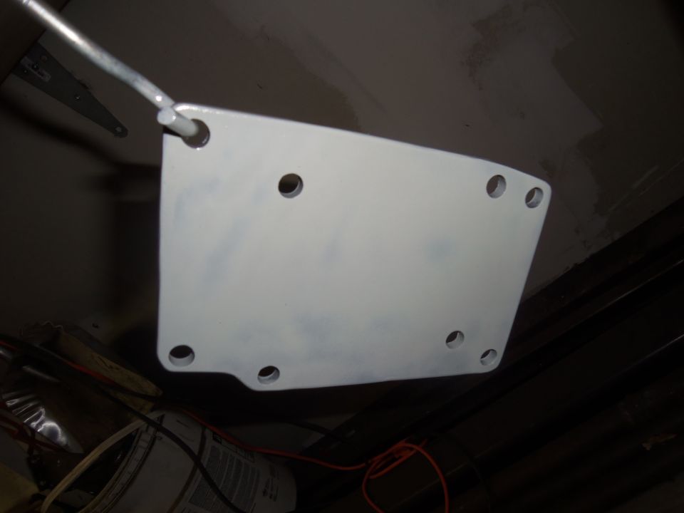 White metal plate with multiple holes, suspended by a rod. Some scuff marks visible