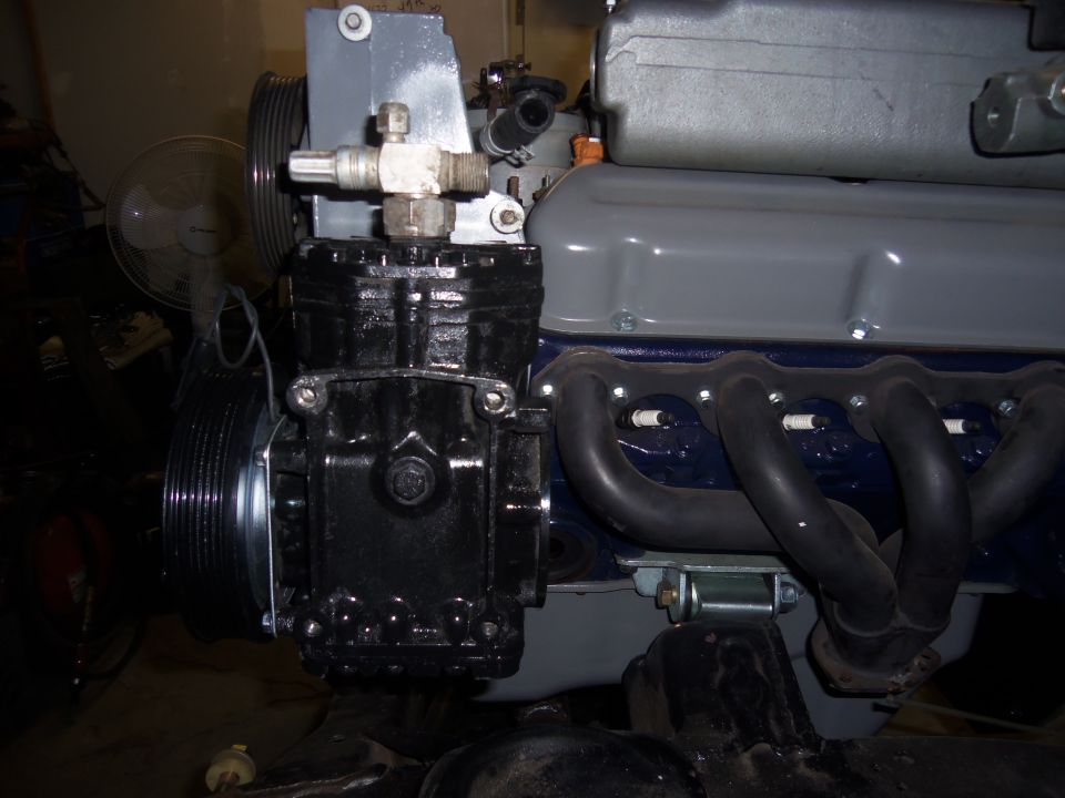Black compressor mounted on engine block with exhaust manifold and pulleys visible