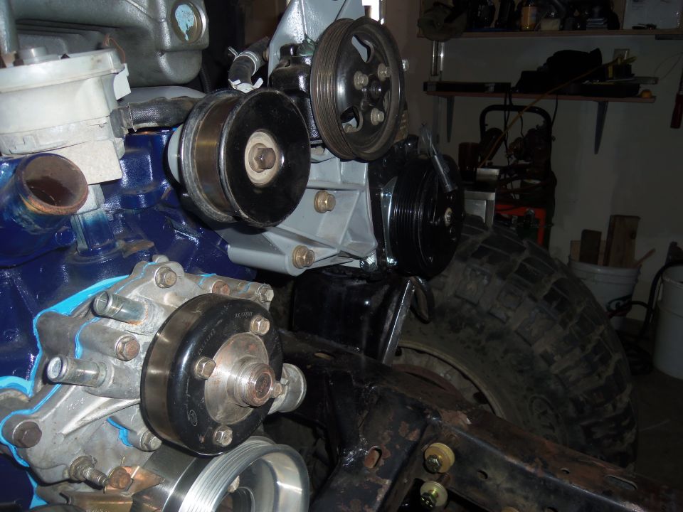 Close-up of engine components and a large tire. Some parts are painted blue and gray
