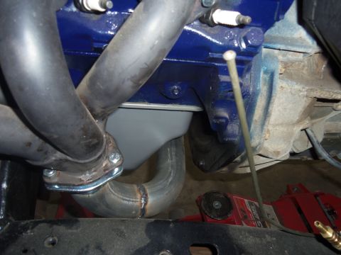 1968 Ford Bronco - Close-up view of an exhaust manifold connected to an engine block, with an oil pan visible below.