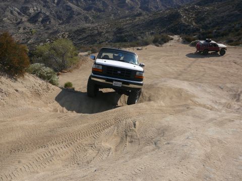 1988 Ford Bronco - A white Ford Bronco navigates a sandy incline, with another off-road vehicle in the background.
