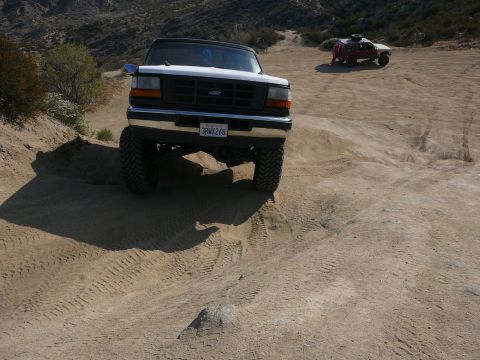 1988 Ford Bronco - White Ford Bronco driving on a dirt trail with another vehicle in the distance.