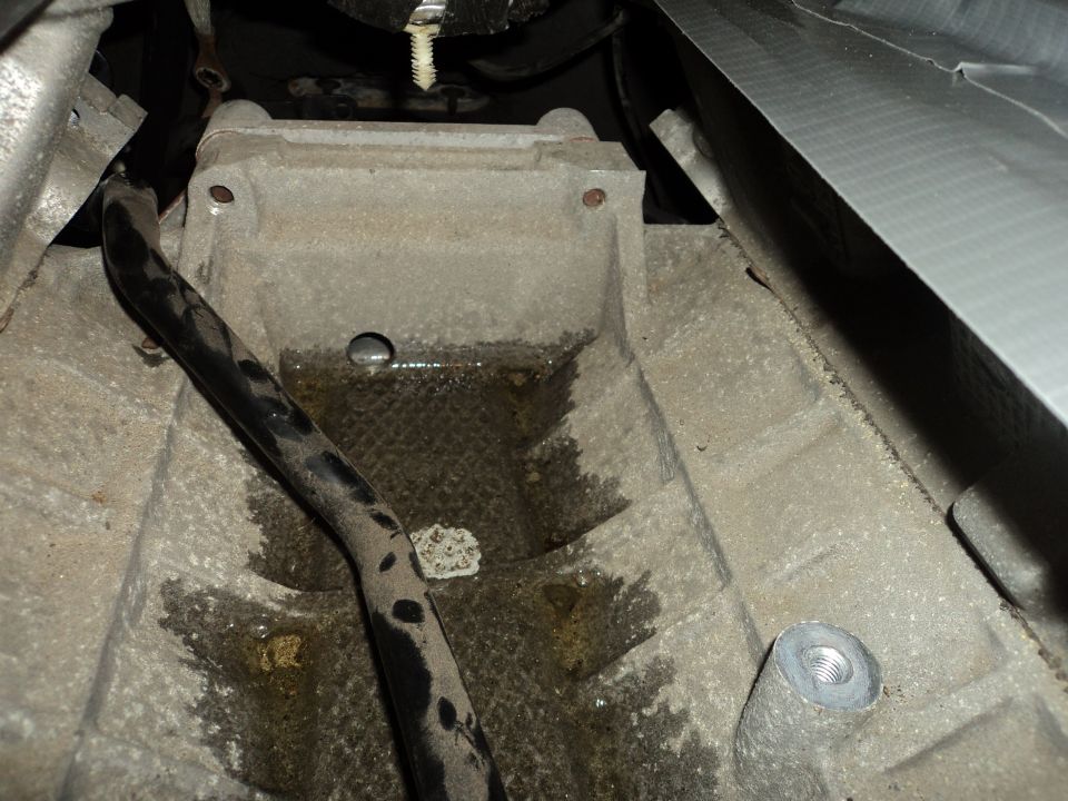 Close-up of a greasy metal casing, possibly engine or transmission, with a black hose and some fluid pooled