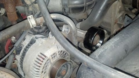 1995 Ford Bronco - Close-up view of a black belt tensioner pulley on an engine, with visible hoses and alternator.