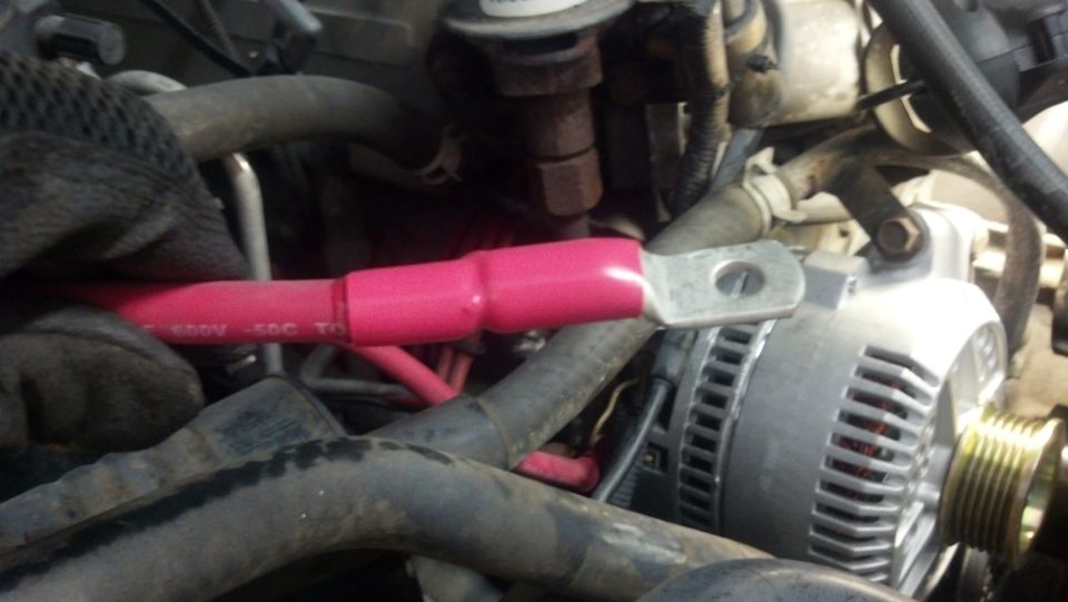 Close-up of a red battery cable being connected to a vehicle's alternator